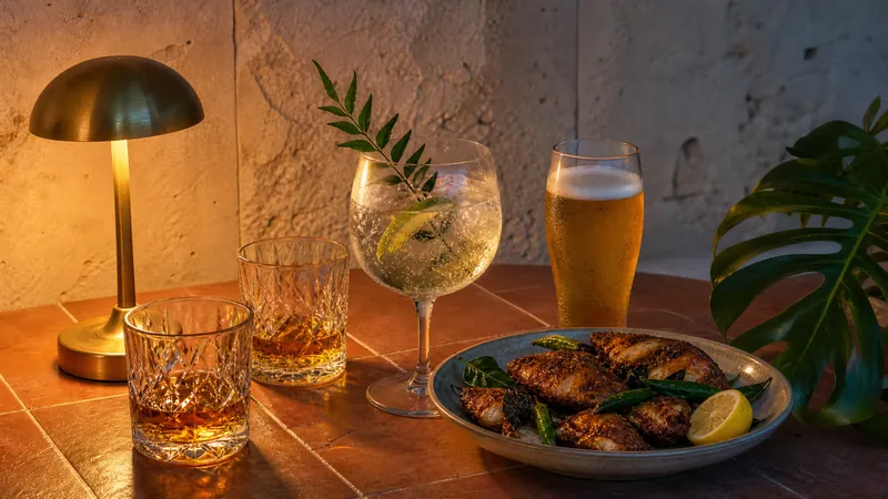 Whisky tumblers, a gin and tonic with curry leaf, a lager and spiced fried fish at dusk.