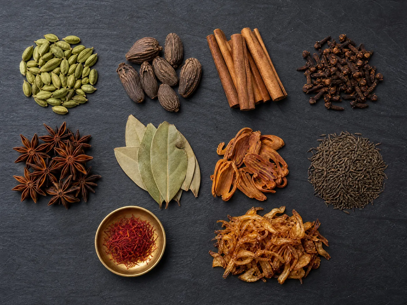 Whole spices for Hyderabadi biryani in small piles on slate.